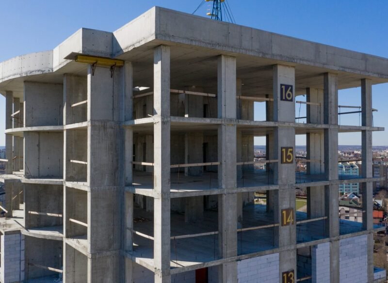 Aerial view of concrete frame of tall apartment building under construction in a city.