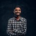 Cheerful hindu guy posing and laughing crossed his arms in the studio on a black background