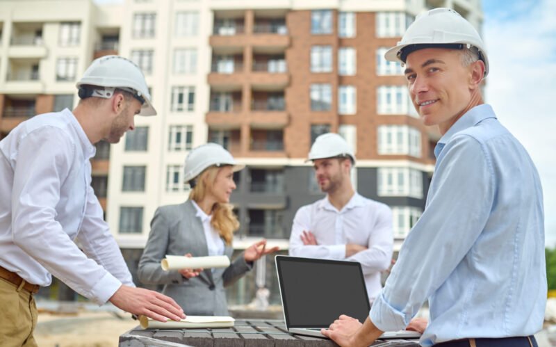 Smiling contented middle-aged engineer posing for the camera with his colleagues on the background